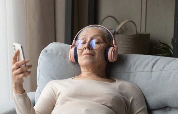 Calm senior lady in wireless headphones listening to relaxing music