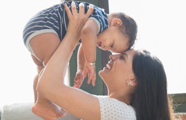 Smiling Hispanic mother lifting baby son Yesil Science Smiling Hispanic mother lifting baby son